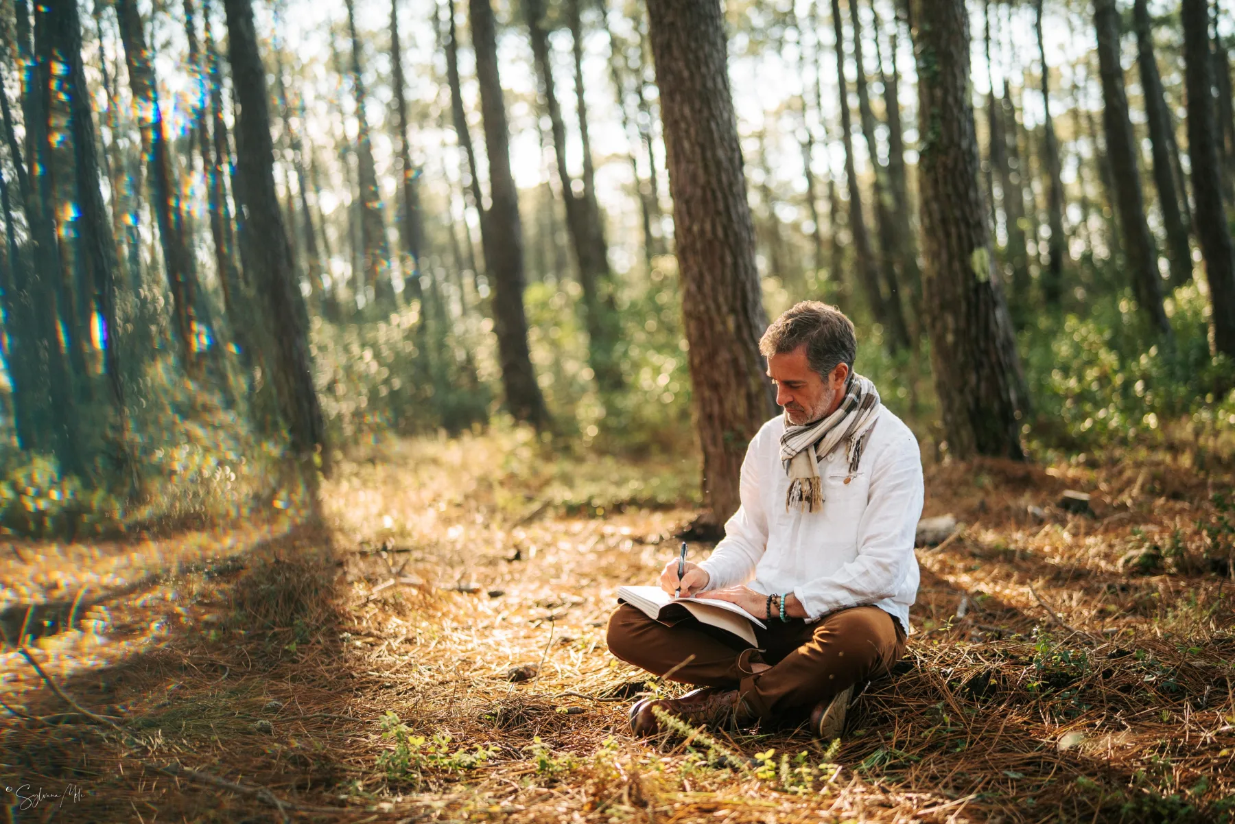 Pierre Lapoujade assis dans une forêt et écrivant dans un carnet